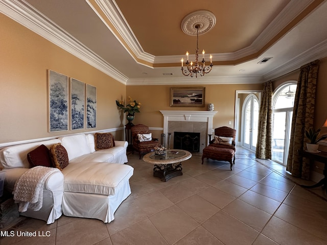 tiled living room with a raised ceiling, a tiled fireplace, ornamental molding, and a chandelier