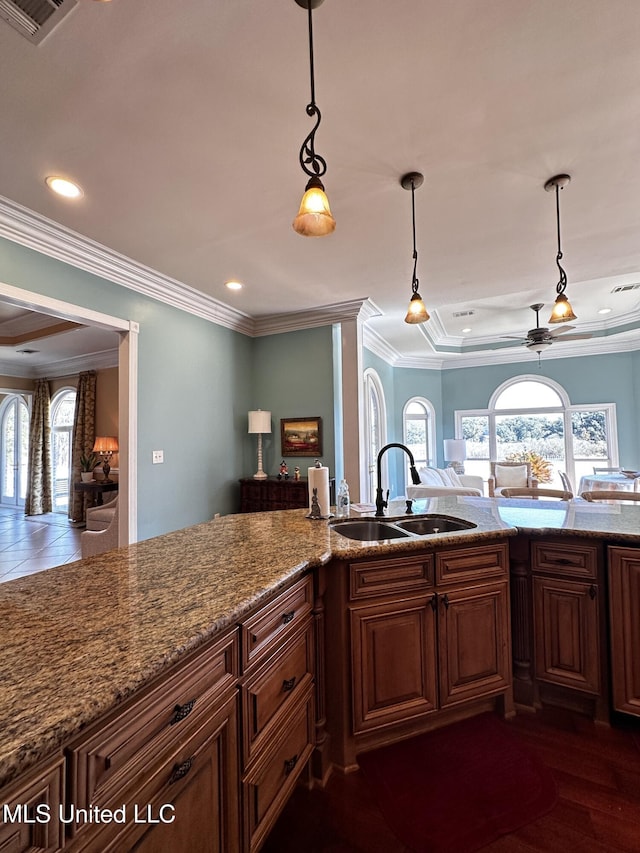 kitchen featuring sink, light stone counters, ornamental molding, pendant lighting, and ceiling fan