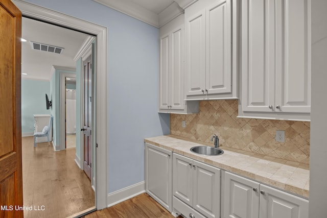 interior space with sink, light hardwood / wood-style floors, white cabinets, light stone counters, and decorative backsplash