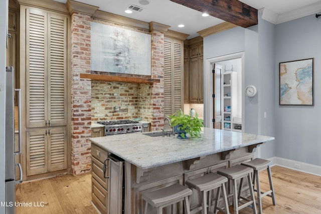 kitchen featuring high end stove, light hardwood / wood-style flooring, a center island with sink, sink, and light stone counters