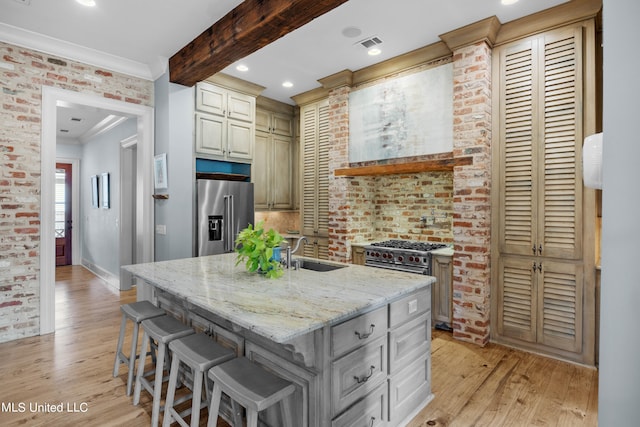 kitchen featuring a kitchen island with sink, high quality appliances, light hardwood / wood-style flooring, sink, and light stone counters