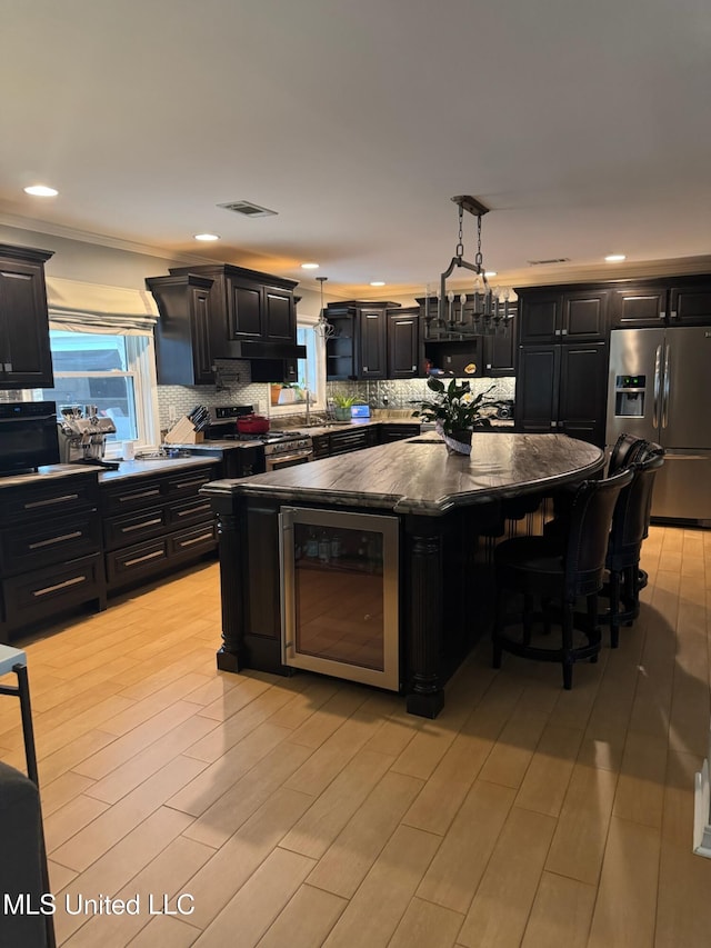 kitchen with dark cabinets, visible vents, appliances with stainless steel finishes, and beverage cooler