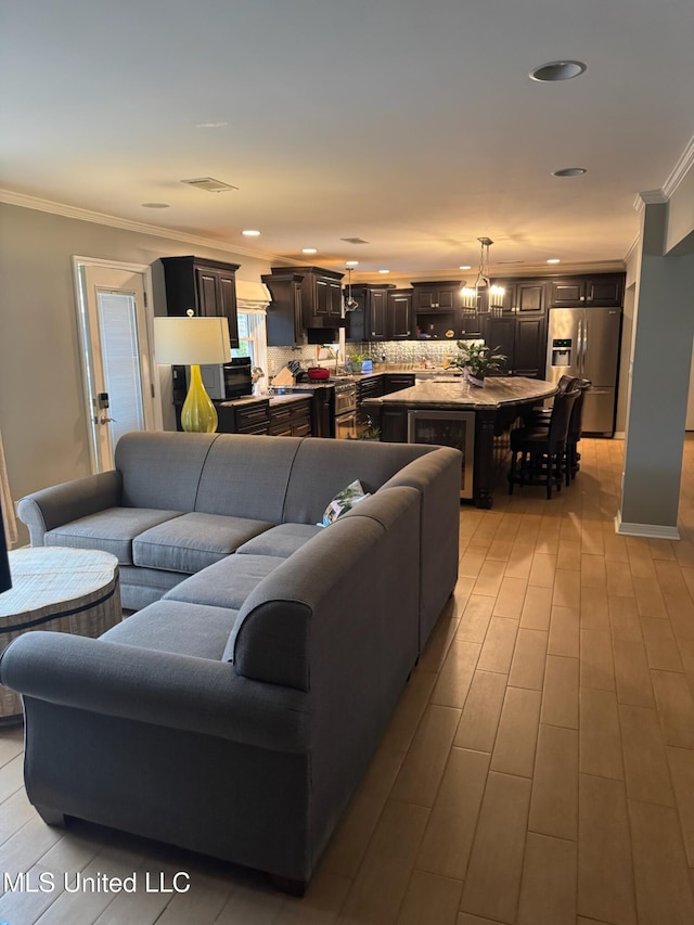 living area with light wood finished floors, visible vents, recessed lighting, and crown molding