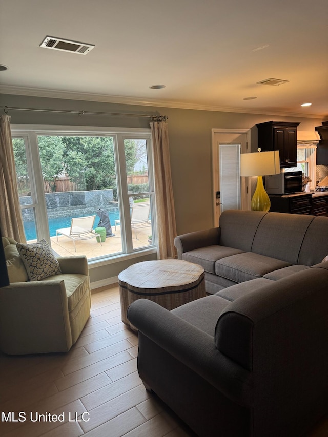 living room with visible vents, light wood-type flooring, and crown molding