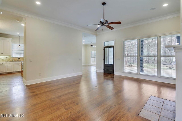 unfurnished living room with a sink, wood finished floors, a ceiling fan, and ornamental molding