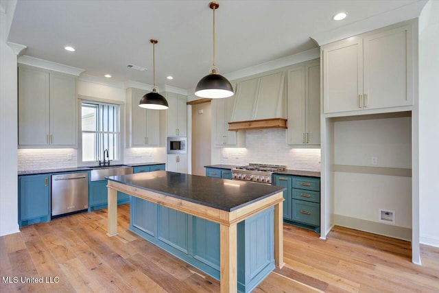 kitchen featuring premium range hood, light wood-style flooring, appliances with stainless steel finishes, blue cabinets, and a sink