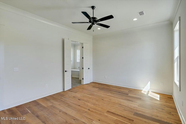 empty room featuring visible vents, plenty of natural light, wood finished floors, and crown molding