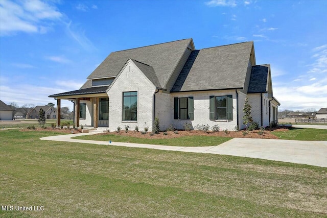 view of front facade with a front yard, brick siding, and a shingled roof