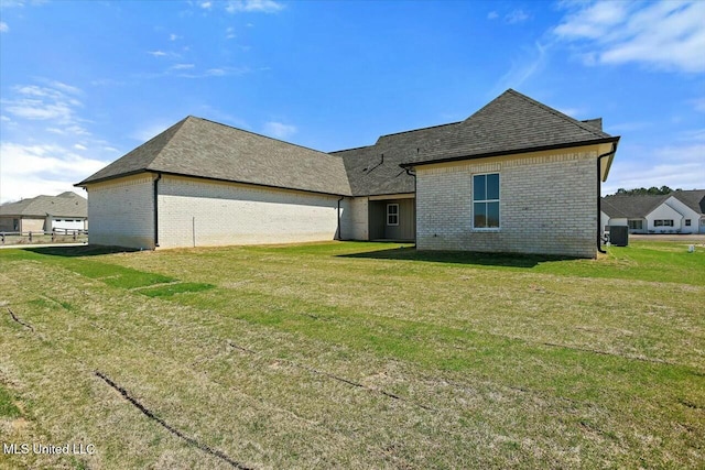 back of house with a yard, brick siding, and roof with shingles