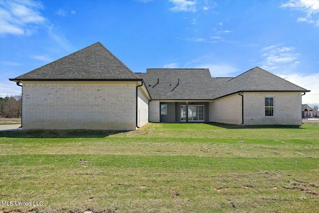 rear view of property with a yard, brick siding, and roof with shingles