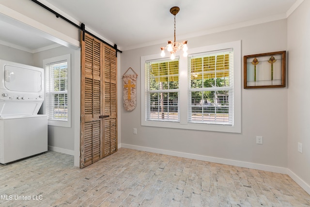 washroom featuring stacked washing maching and dryer, crown molding, light hardwood / wood-style flooring, and a barn door