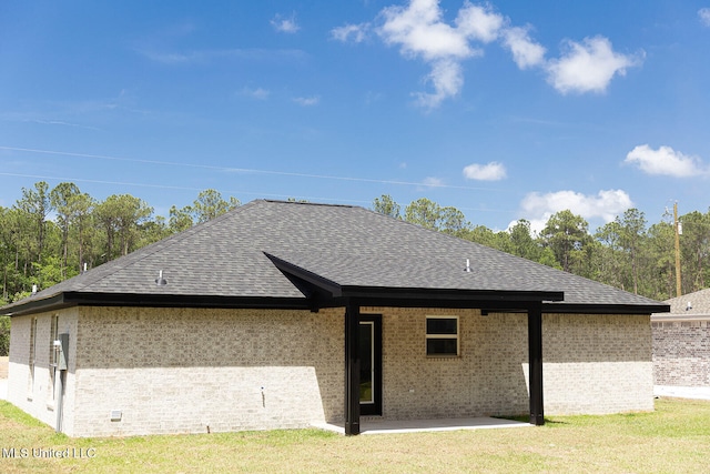 rear view of property featuring roof with shingles, brick siding, a lawn, and a patio