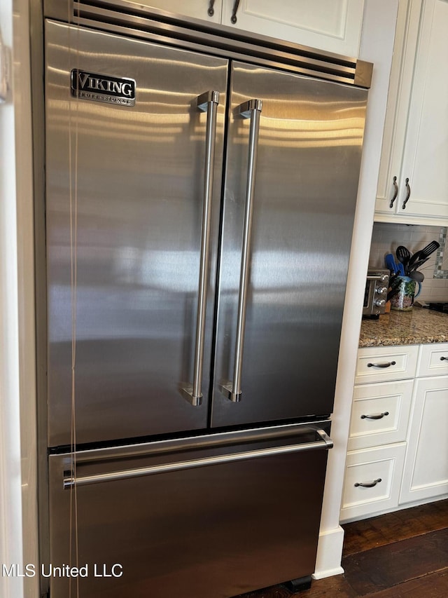 details featuring stainless steel built in refrigerator, dark stone countertops, white cabinets, dark hardwood / wood-style flooring, and backsplash