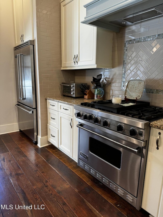 kitchen with custom exhaust hood, high end appliances, dark hardwood / wood-style flooring, light stone countertops, and backsplash