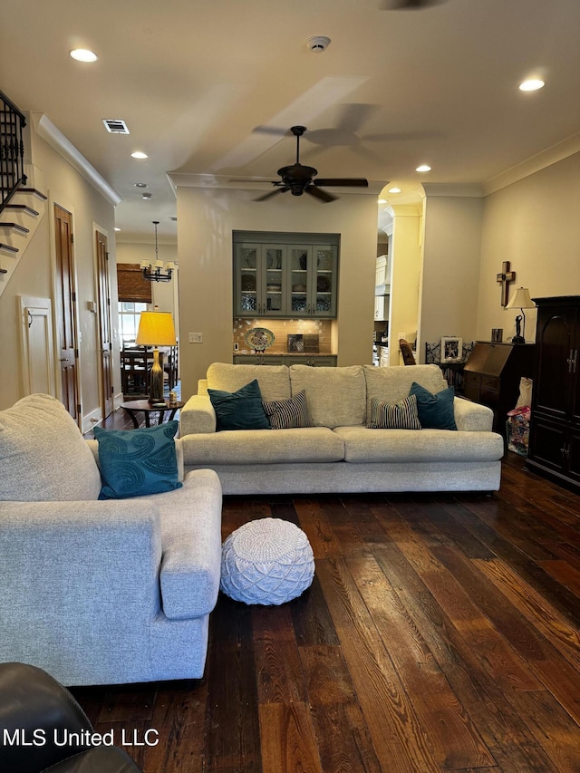 living room featuring dark wood-type flooring, crown molding, and ceiling fan with notable chandelier