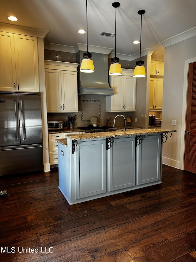 kitchen with premium range hood, decorative light fixtures, a center island with sink, high quality fridge, and light stone countertops