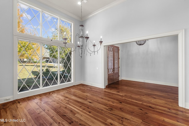 unfurnished dining area with a chandelier, a towering ceiling, dark wood-type flooring, and ornamental molding