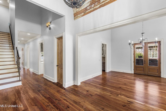 foyer entrance with french doors, ornamental molding, dark wood-type flooring, an inviting chandelier, and a high ceiling