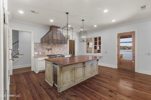 kitchen with premium range hood, a kitchen island with sink, dark hardwood / wood-style floors, and wood counters