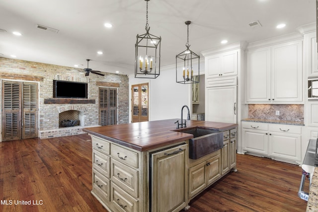 kitchen featuring wooden counters, sink, white cabinets, dark hardwood / wood-style floors, and an island with sink