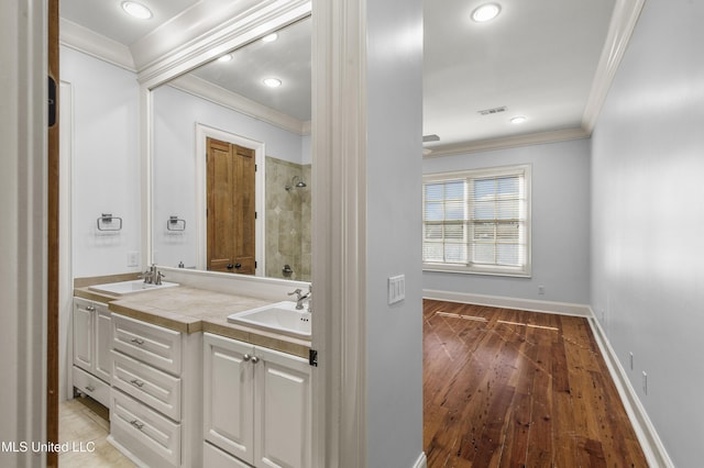 bathroom featuring hardwood / wood-style floors, vanity, a tile shower, and ornamental molding