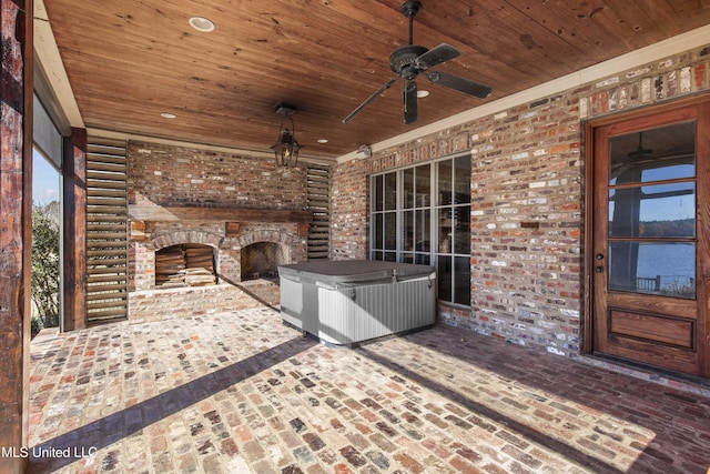 view of patio with an outdoor brick fireplace, ceiling fan, and a hot tub