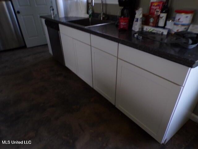kitchen featuring stainless steel dishwasher, dark countertops, white cabinets, and a sink