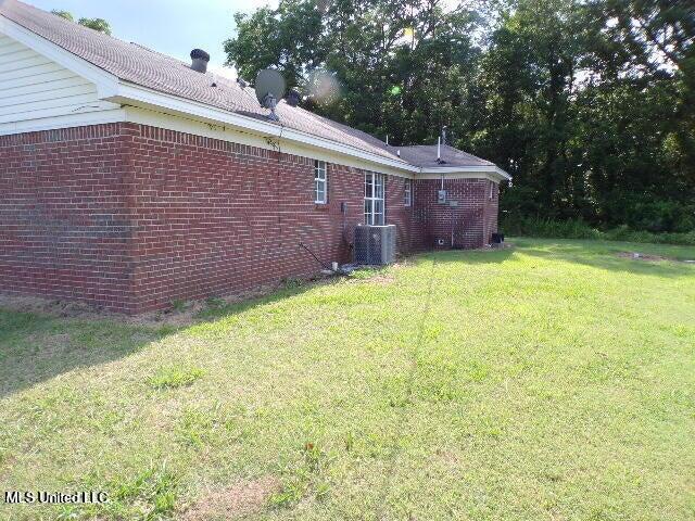 view of side of home with brick siding, central AC, and a yard