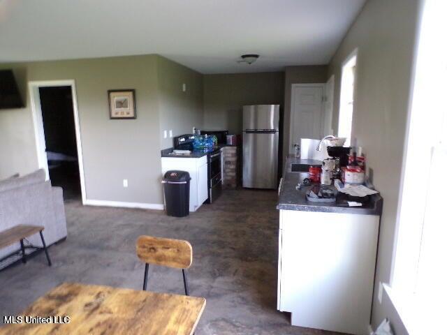 kitchen with range, a sink, dark countertops, freestanding refrigerator, and white cabinets