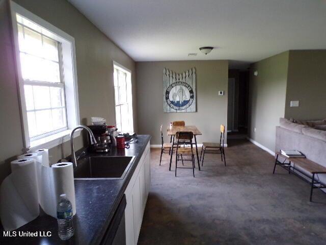 kitchen with white cabinetry, baseboards, a sink, dark countertops, and dishwashing machine