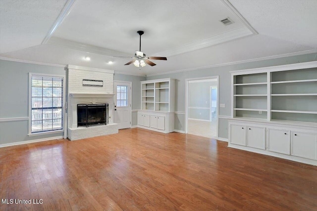 unfurnished living room with light wood-type flooring, a fireplace, a raised ceiling, ceiling fan, and ornamental molding