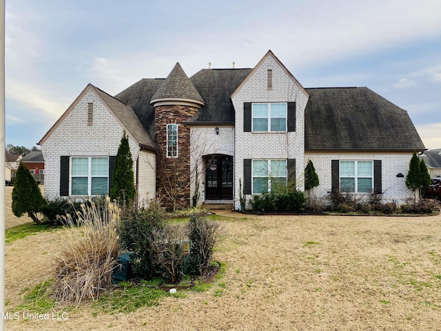 french provincial home with brick siding, a front yard, and a shingled roof