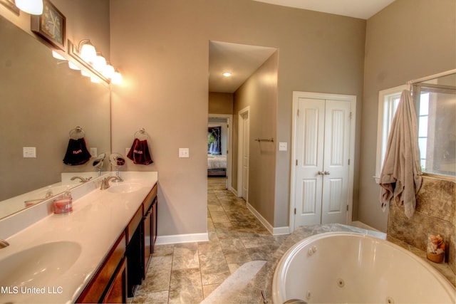 ensuite bathroom featuring double vanity, ensuite bathroom, a sink, a jetted tub, and baseboards