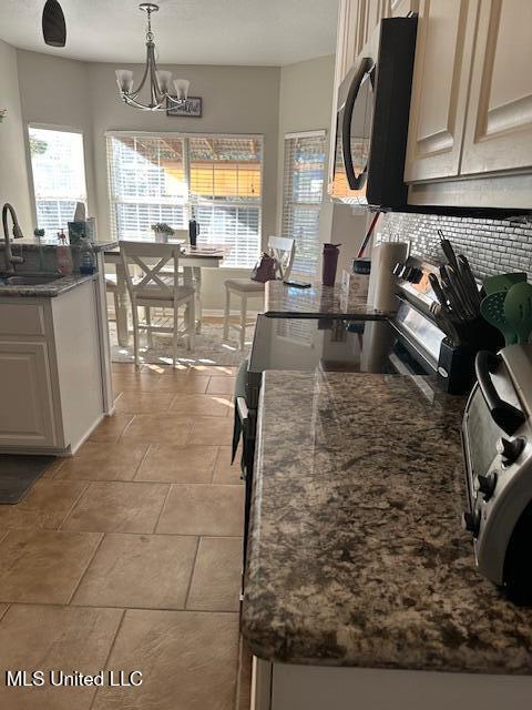 kitchen featuring stove, tasteful backsplash, sink, pendant lighting, and a notable chandelier