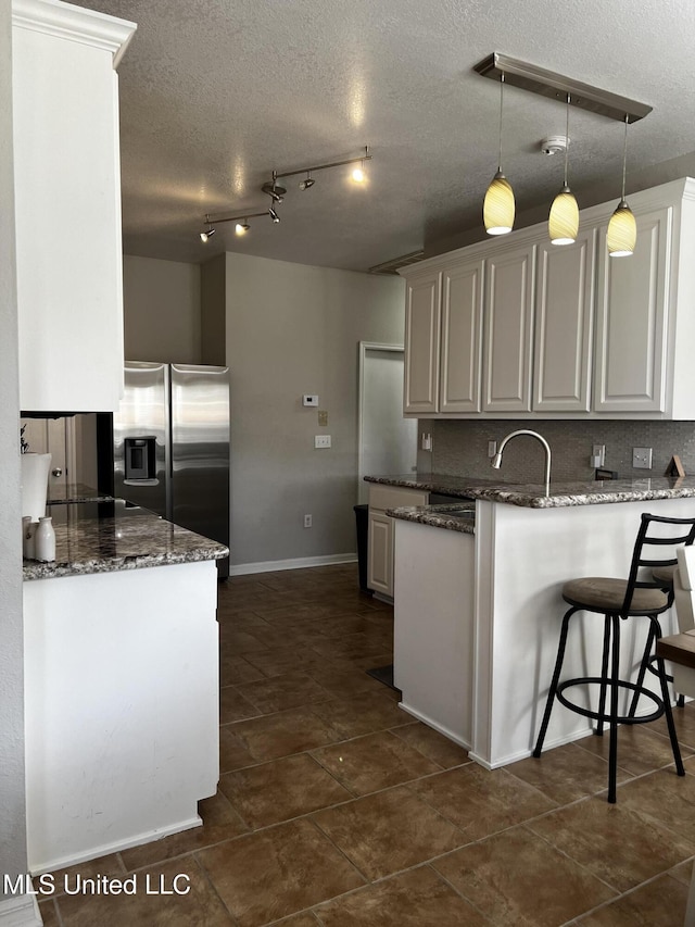 kitchen featuring dark stone countertops, stainless steel fridge, white cabinets, and a textured ceiling