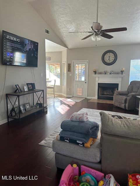 living room with ceiling fan, dark wood-type flooring, a textured ceiling, and vaulted ceiling