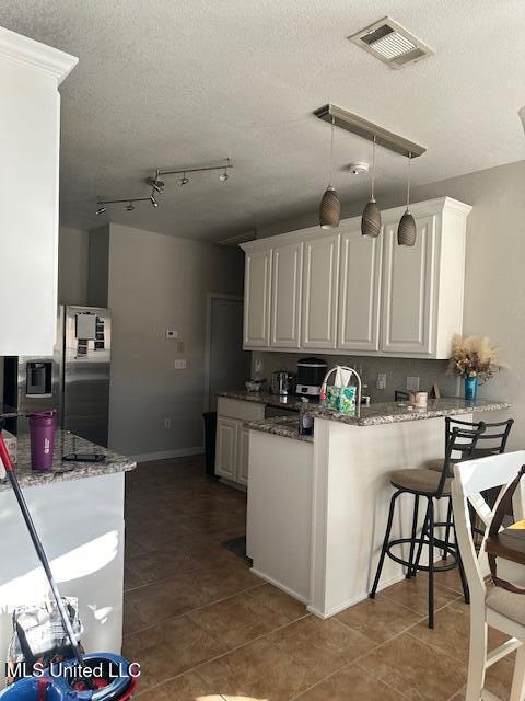 kitchen with kitchen peninsula, white cabinetry, hanging light fixtures, and stone countertops