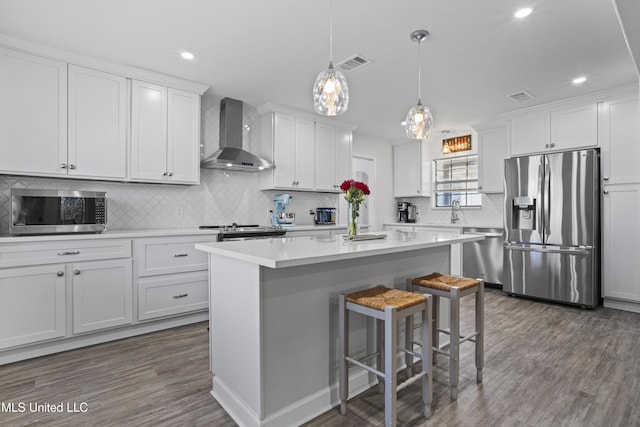 kitchen featuring stainless steel appliances, white cabinetry, wall chimney range hood, and a kitchen breakfast bar