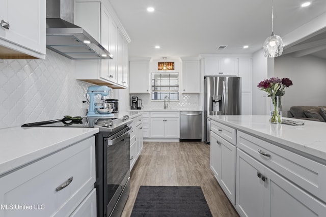 kitchen with appliances with stainless steel finishes, light wood-type flooring, white cabinetry, and wall chimney range hood