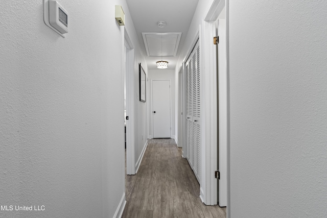 hall with attic access, baseboards, wood finished floors, and a textured wall