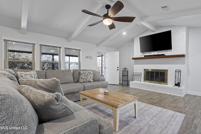 living room featuring vaulted ceiling with beams, wood finished floors, visible vents, baseboards, and a brick fireplace