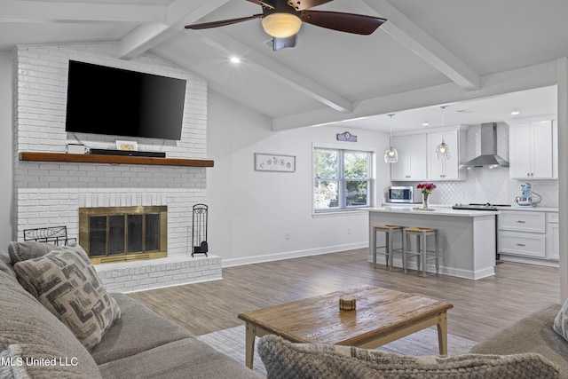 living room featuring vaulted ceiling with beams, a fireplace, light wood-style flooring, and baseboards