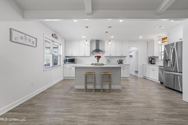 kitchen with decorative backsplash, wall chimney exhaust hood, appliances with stainless steel finishes, beamed ceiling, and white cabinetry