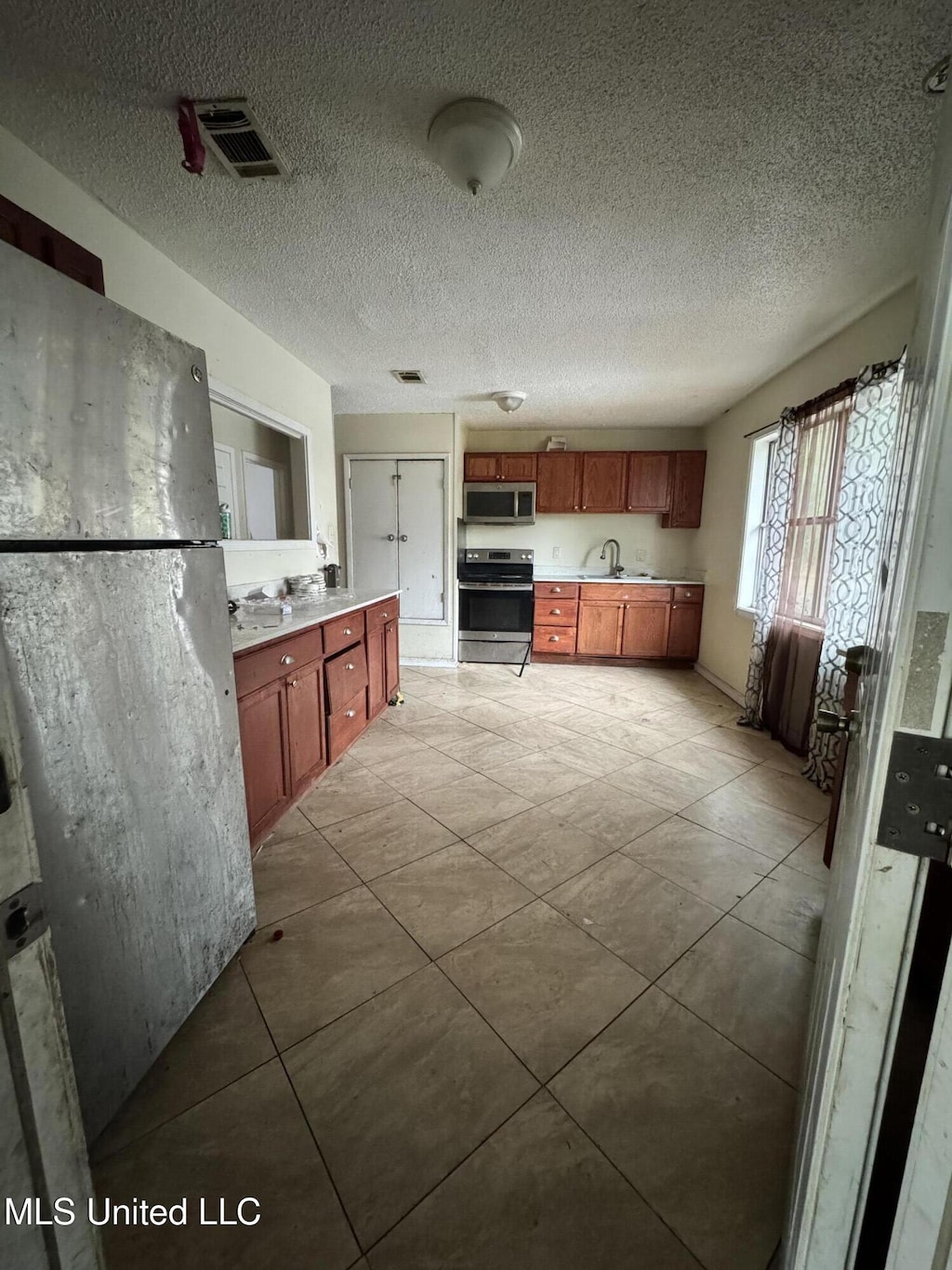 kitchen featuring sink, light tile patterned floors, stainless steel appliances, and a textured ceiling