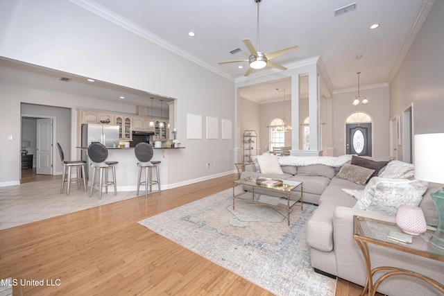 living room with ceiling fan with notable chandelier, a towering ceiling, ornamental molding, and light hardwood / wood-style floors