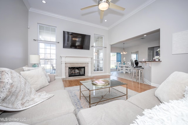 living room featuring hardwood / wood-style floors, ceiling fan with notable chandelier, ornamental molding, and a brick fireplace