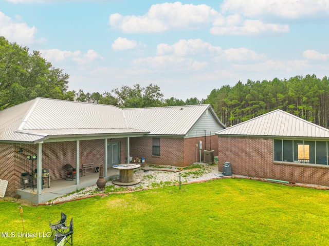 rear view of property featuring brick siding, a lawn, a patio area, metal roof, and cooling unit