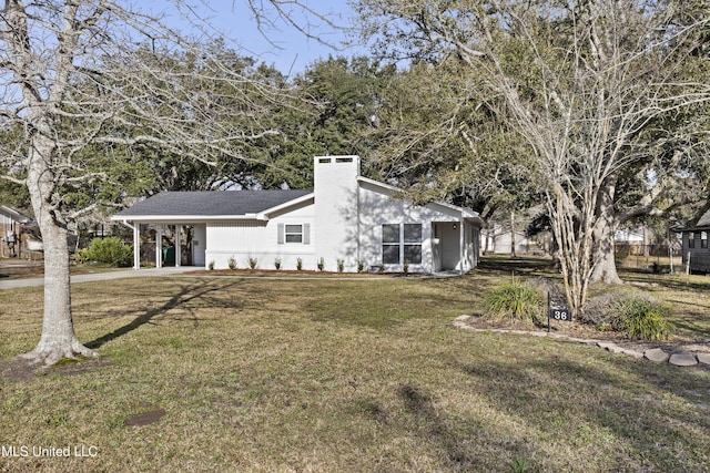 view of side of home featuring concrete driveway, a chimney, a carport, and a yard