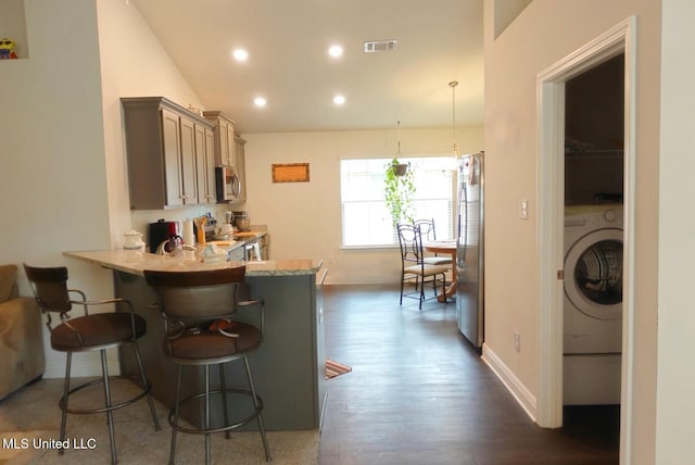 kitchen featuring visible vents, a kitchen breakfast bar, appliances with stainless steel finishes, dark wood-style floors, and washer / dryer