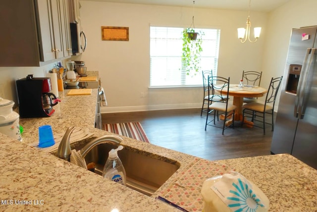 kitchen with dark wood-type flooring, a sink, appliances with stainless steel finishes, light stone countertops, and pendant lighting